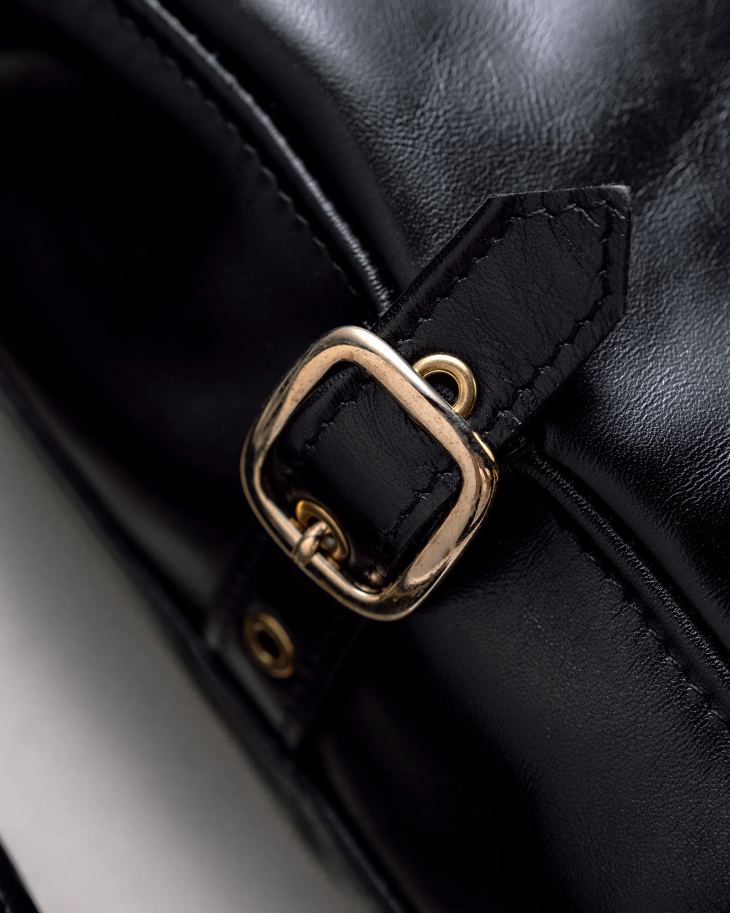 Detail shot of polished brass buckle on black horsehide leather jacket. See product details for more information.