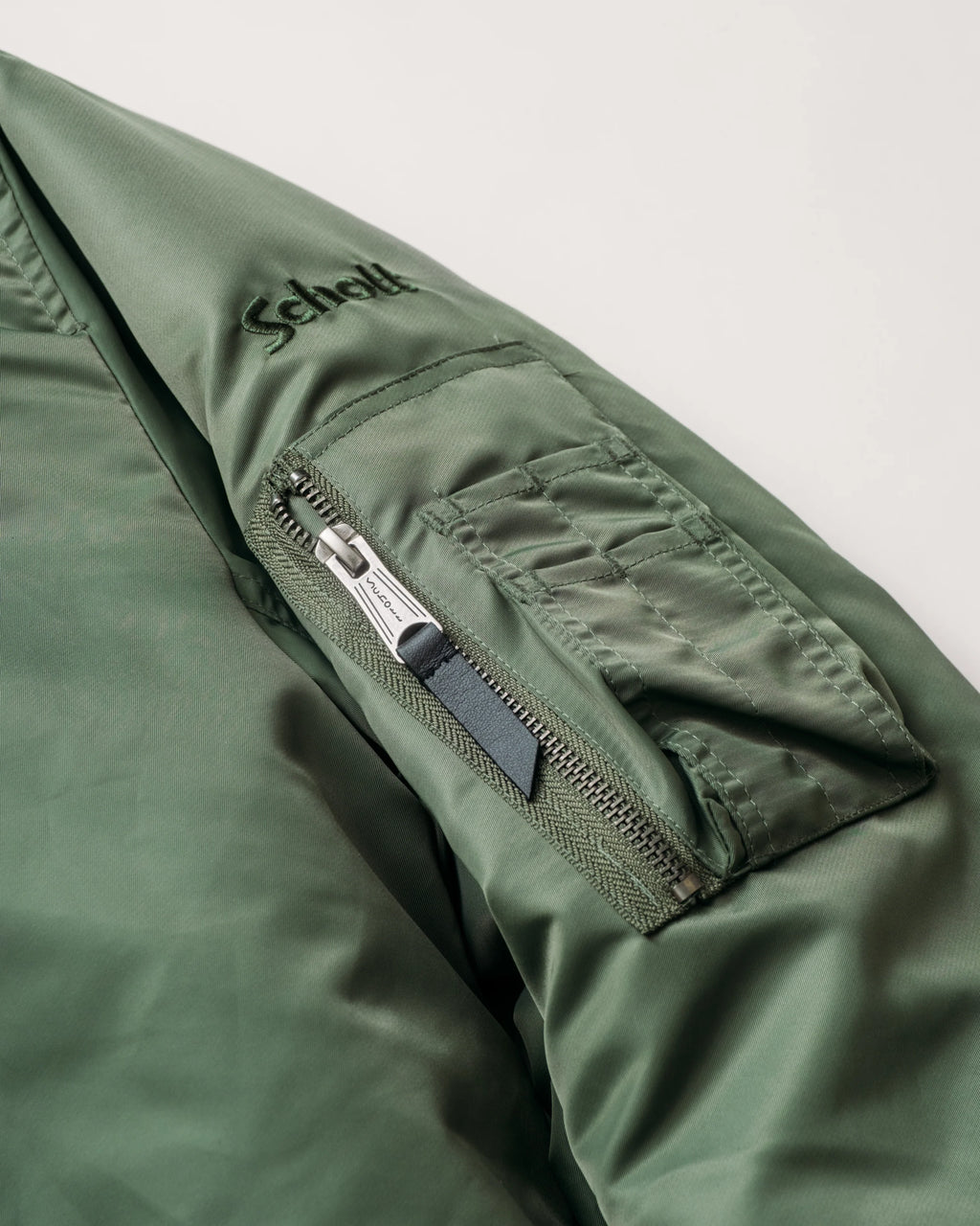 Zip arm pocket and tonal Schott logo embroidery detail shot of sage bomber jacket. See product details for more information.